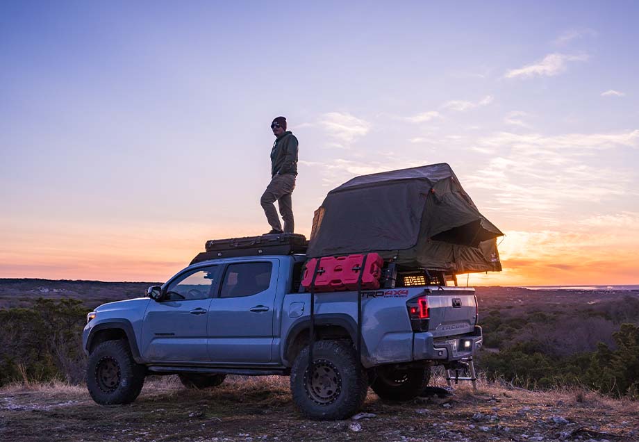 Man on top with installed Tent and Cali Raised Overland Bed Rack | 2005-2023 Toyota Tacoma